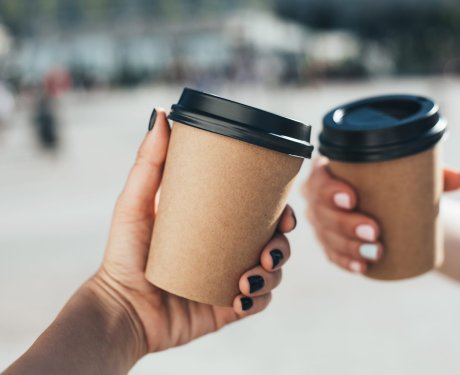 Two women holding paper coffee cups in front of a city.