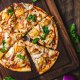 Pizza topped with pineapple, chicken, red onion, and cilantro on a wooden board, with cilantro leaves scattered around.