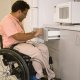 A man in a wheelchair accessing a microwave placed on a lower cabinet in an accessible kitchen.