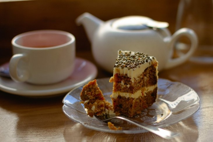 A piece of cake on a plate next to a cup of tea.