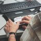 A person using a braille display and keyboard on a desk, with focus on their hands and wrists.