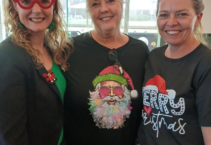 Three women smiling, two wearing Christmas-themed shirts and one with reindeer glasses.