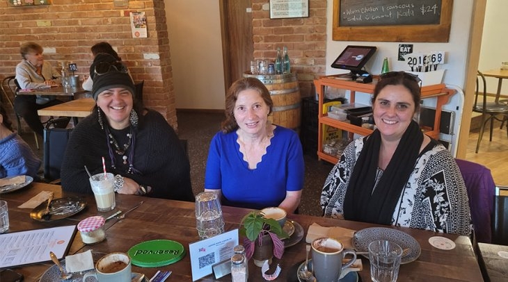 Three female NDIS participant out at an Enhanced Lifestyles Lunch, laughing sitting next to each other smiling and laughing