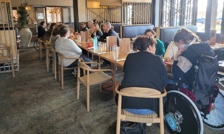 NDIS Participants and their Disability Support workers at customer event sitting at a long table enjoying coffee, and cakes.