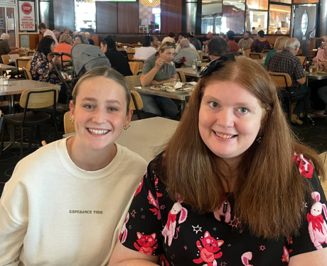 Two women smiling at the camera in a busy restaurant.