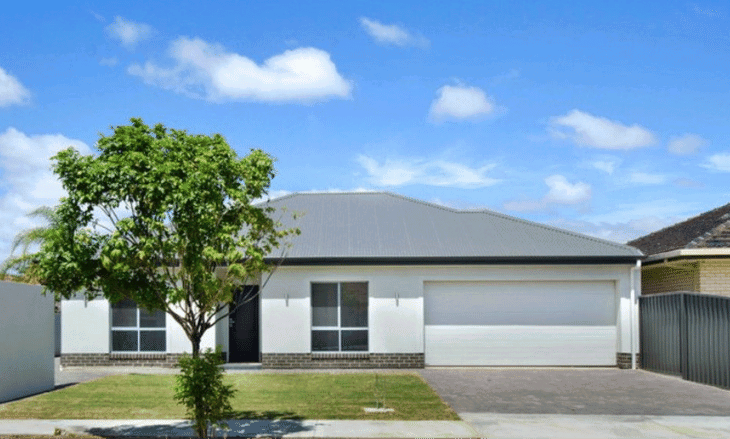 Outside of the NDIS SIL house, house is modern with white rendering and a grey iron roof, with a large square of lawn to the left side and a double garage to the right.