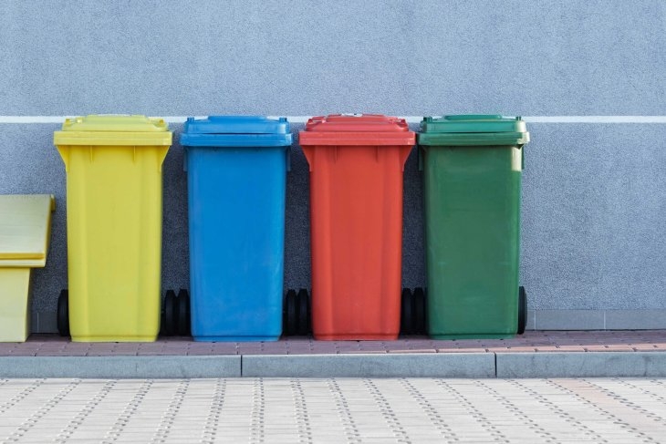 A row of colorful trash cans next to a wall.