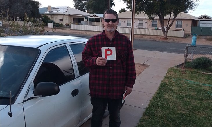 Male NDIS participant standing next to his car proudly holding his P plate