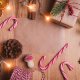 A festive arrangement on a wooden surface with candy canes, a wrapped gift, dried orange slices, pinecones, and holiday lights.