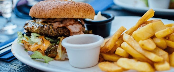 A beef burger in a bun with bacon and lettuce, fries, a pot of mayonnaise and another pot that you can’t see into but probably contains tomato sauce