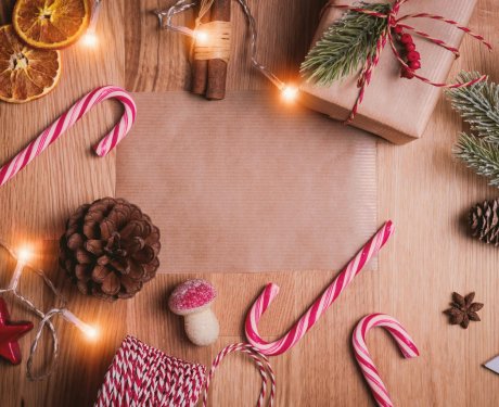 A festive arrangement on a wooden surface with candy canes, a wrapped gift, dried orange slices, pinecones, and holiday lights.